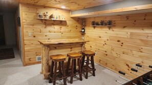A wooden bar area with stools, shelves with bottles, and a small house model. - Devil’s Lake 5BR Cabin w/ Fireplaces,King beds,Skiing* Near Water parks in Dells (Baraboo)