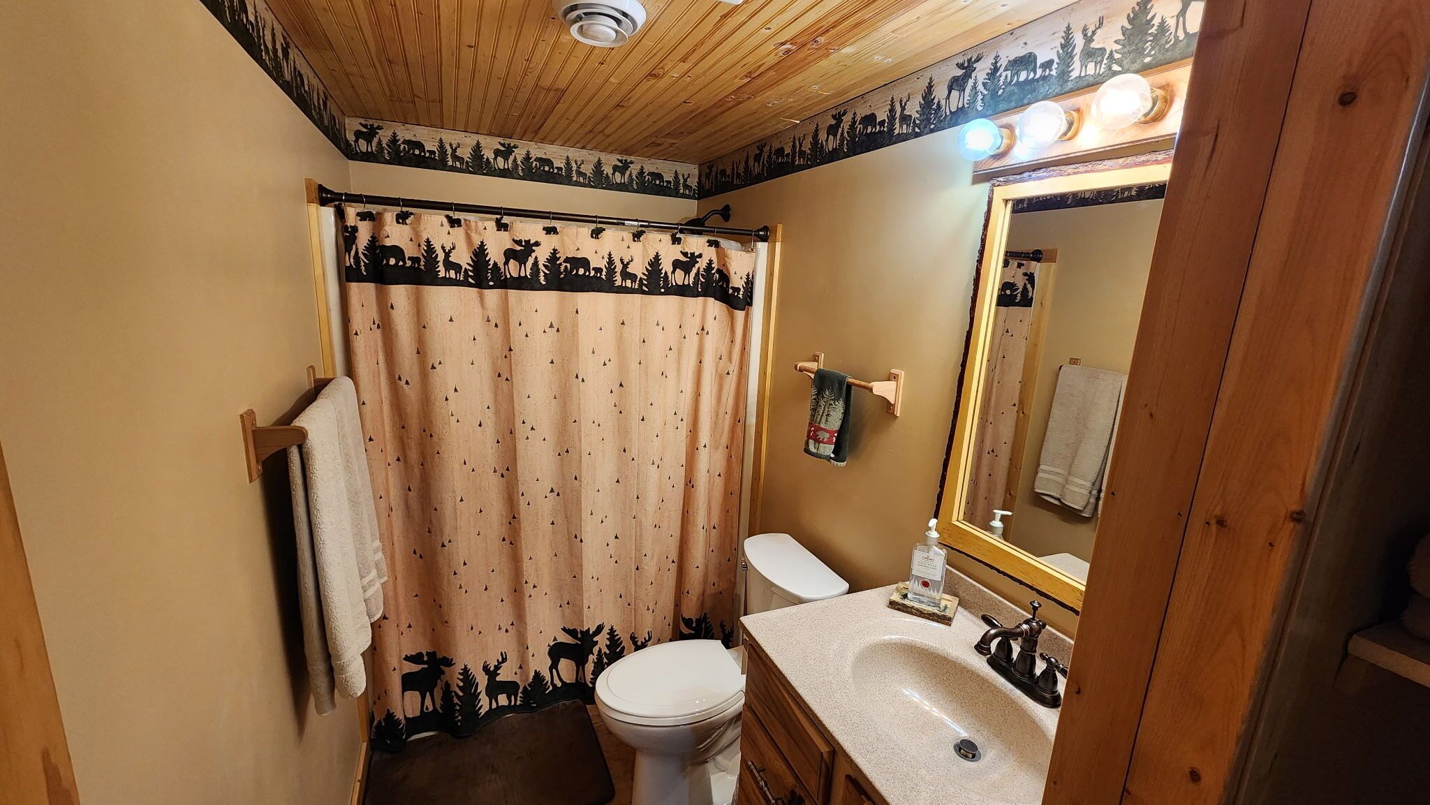 A bathroom with a shower curtain featuring animal silhouettes, a toilet, a sink with a mirror, and a towel rack.