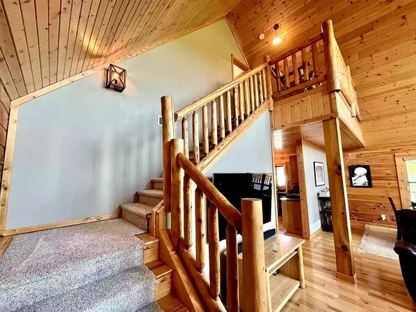 A wooden interior with a staircase, a flat-screen TV, and a kitchen area. - Devil’s Lake 5BR Cabin w/ Fireplaces,King beds,Skiing* Near Water parks in Dells (Baraboo)
