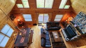 Un intérieur de chalet chaleureux avec un plancher en bois, une cheminée, un canapé, une table à manger et un mur décoratif en pierre.