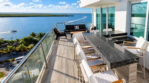 A balcony with a view of a body of water, outdoor seating, and a modern kitchen area.