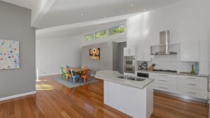 A modern kitchen with white cabinets, a granite countertop, and stainless steel appliances. - At The Beach - Great Family House (North Avoca)