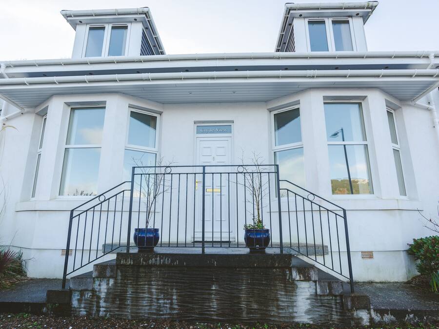 Ein zweistöckiges Haus mit weißer Fassade, einer Haustür und einer kleinen Veranda mit Metallgeländer.