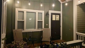 Un porche cubierto con una mesa, sillas, una puerta y luces colgantes.