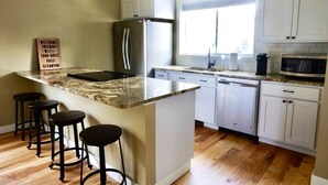 Una cocina con una isla central, taburetes de bar, refrigerador, microondas y armarios blancos.