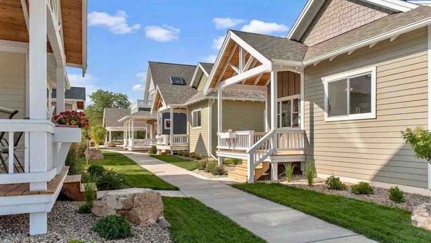 Una hilera de casas de un piso con porches adosados, cielo despejado y un césped bien cuidado.