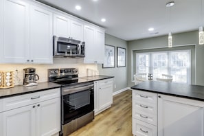 A modern kitchen with white cabinetry, stainless steel appliances, and a large window providing natural light. - Sunset Rentals | Evian 170 (Hilton Head Island)