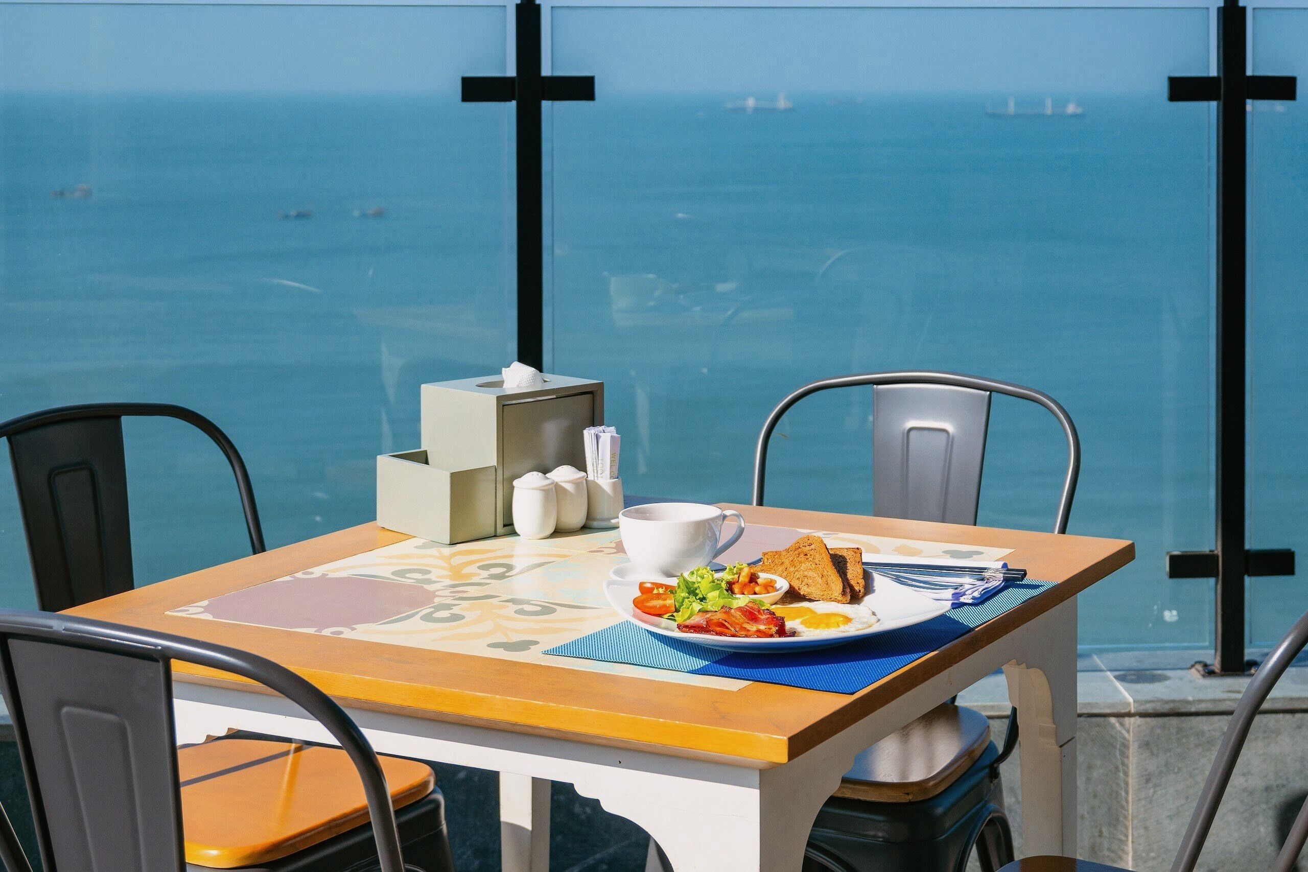 A table with breakfast, a cup, and a view of the sea.
