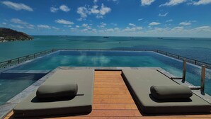 An infinity pool with two lounge chairs facing the ocean, surrounded by a wooden deck. - Skool Plus Vung Tau (Ho Chi Minh City)