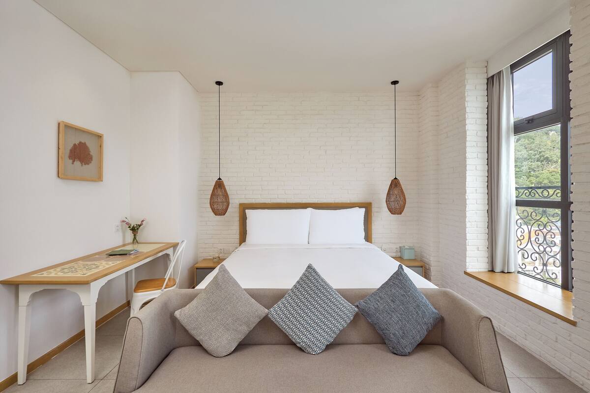 Een slaapkamer met een bed, nachtkastje en een raam met uitzicht.