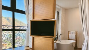 A modern bathroom with a large window, a flat-screen TV, a freestanding bathtub, and a wooden vanity. - Skool Plus Vung Tau (Ho Chi Minh City)