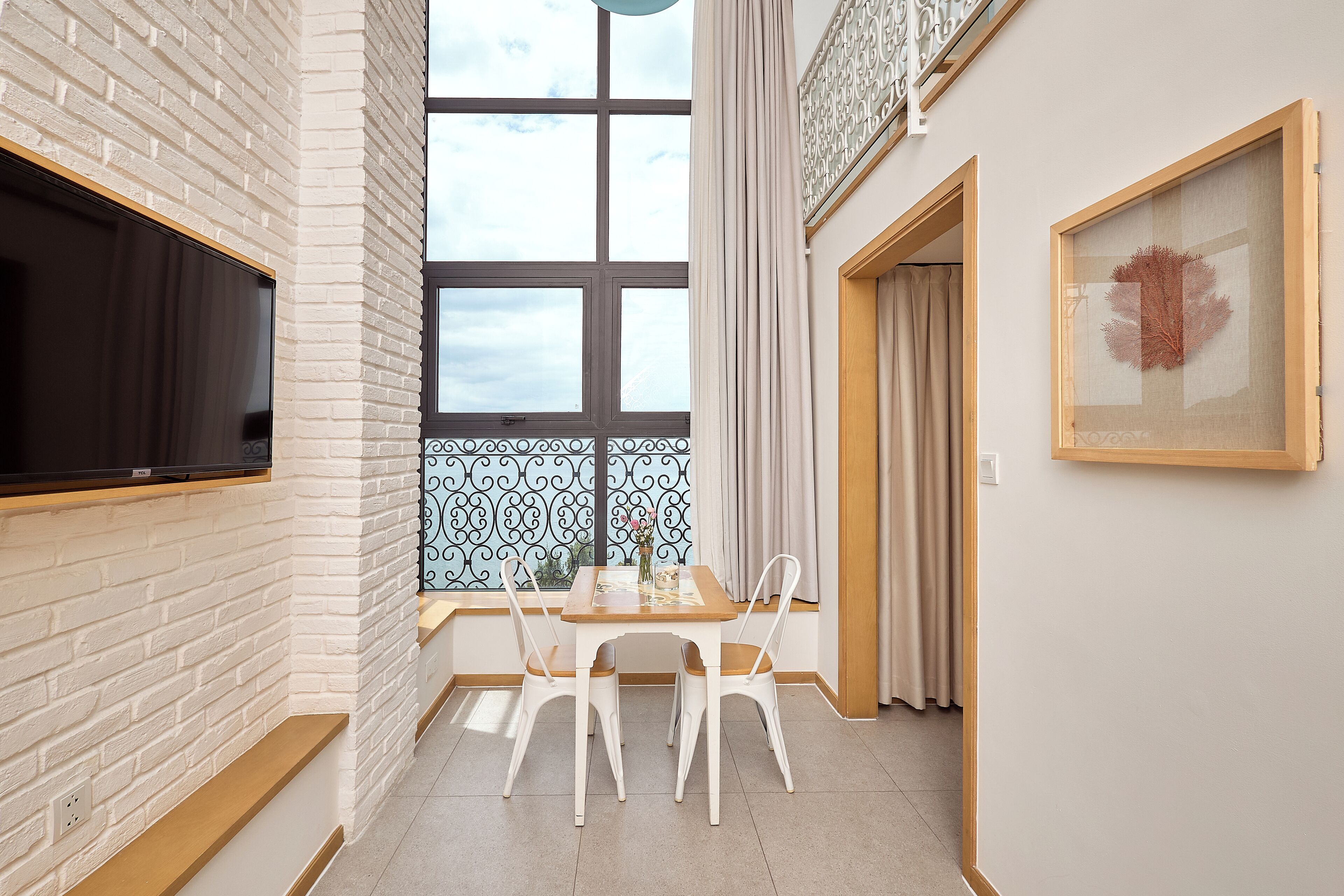 A modern kitchen with white brick walls, a large window with a view, and a dining area with white chairs and a wooden table.