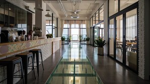 A modern hotel lobby with a central glass walkway, a reception area with bar stools, and large windows offering views of the outdoors. - Skool Plus Vung Tau (Ho Chi Minh City)