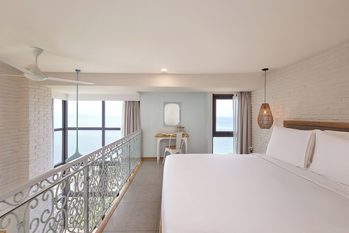 A hotel room with a bed, a desk, and a view of the sea.