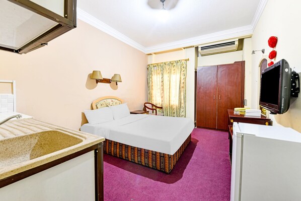 A hotel room with a bed, a desk, a television, and a window with curtains.
