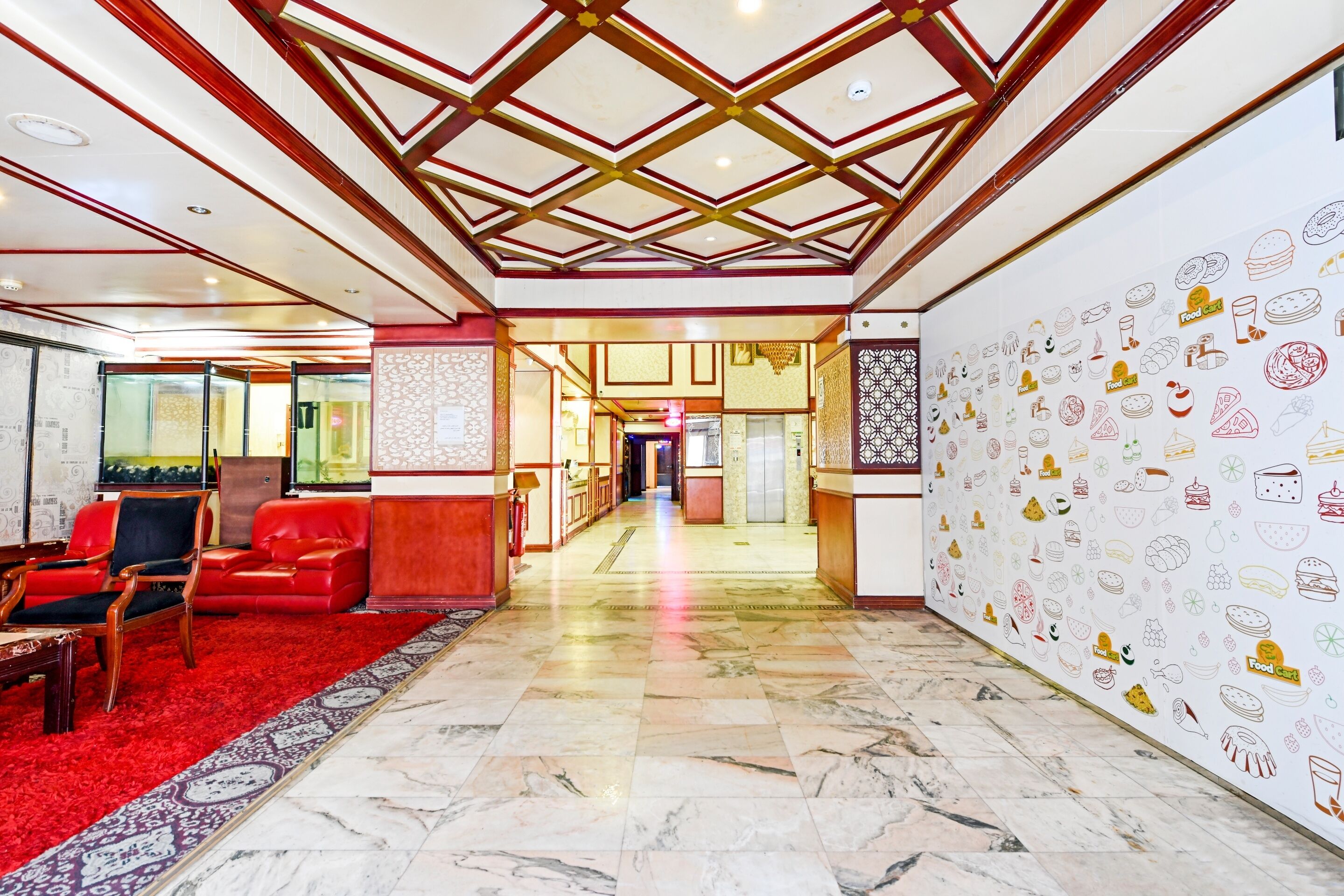 A hotel lobby with a red carpet, wooden furniture, a patterned wall, and a ceiling with a geometric design.