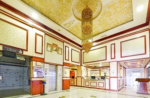 A spacious lobby with a grand chandelier, a reception desk, and a modern elevator.