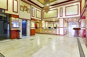 A spacious lobby with marble flooring, a central reception desk, and a chandelier.