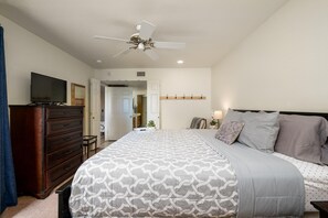 Une chambre à coucher avec un lit, une commode, un ventilateur de plafond et un téléviseur posé sur la commode.