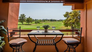 Ein Balkon mit Tisch und zwei Stühlen mit Blick auf einen Golfplatz.