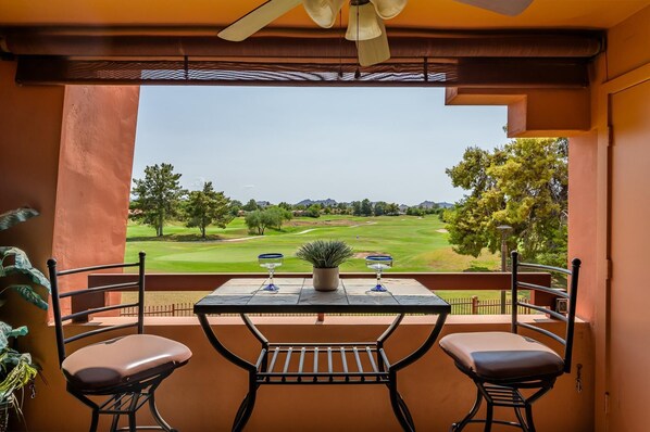 Un balcon avec une table et deux chaises, donnant sur un terrain de golf.
