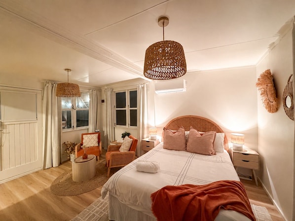 A bedroom with a bed, two nightstands, a chair, a round table, and a hanging light fixture.