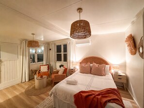 Un dormitorio con una cama, dos mesitas de noche, una silla, una mesa redonda y una lámpara colgante.