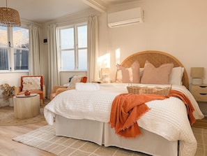 Une chambre avec un grand lit, une table de chevet, une chaise, une fenêtre avec des rideaux et un appareil de climatisation.