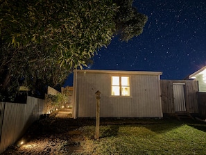 A small wooden shed with a window, surrounded by a fence and a tree.