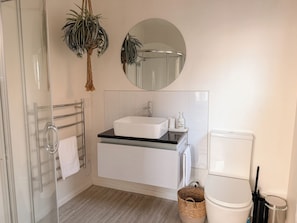 Un baño con lavamanos blanco, un espejo, toallero, inodoro y una planta.
