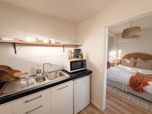 Une cuisine compacte équipée d’un micro-ondes, d’un évier et de placards, qui donne sur une chambre avec un lit et un luminaire suspendu.