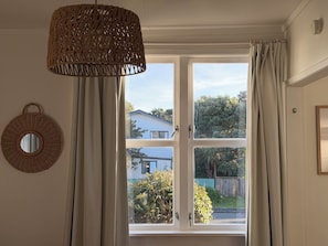 Une pièce dotée d’une grande fenêtre, d’un luminaire en fibres tressées et d’un miroir rond accroché au mur.