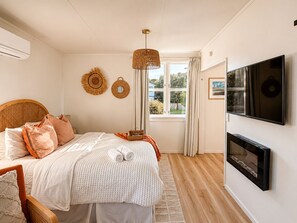 Une chambre à coucher avec un lit, une télévision, une cheminée et une fenêtre avec des rideaux.
