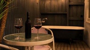Une petite table ronde avec deux verres à vin et une bouteille, une baignoire et un plafond en bois avec des luminaires.