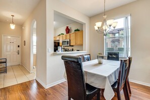 A dining area with a table set for four, wooden chairs, a chandelier, and a view of the kitchen through an archway.