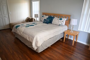 A bedroom with a large bed, a wooden nightstand, a chair, and a window with curtains.