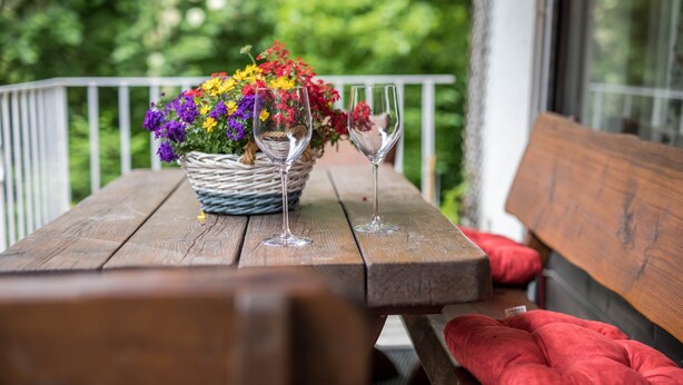 Uma mesa de madeira com uma cesta de vime cheia de flores coloridas e duas taças de vinho vazias.
