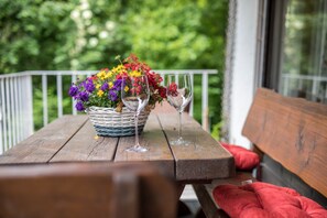 A wooden table with a wicker basket of colorful flowers and two empty wine glasses. - Cosy Holiday Apartment Lilly in Alpine Style with Mountain View (Garmisch)