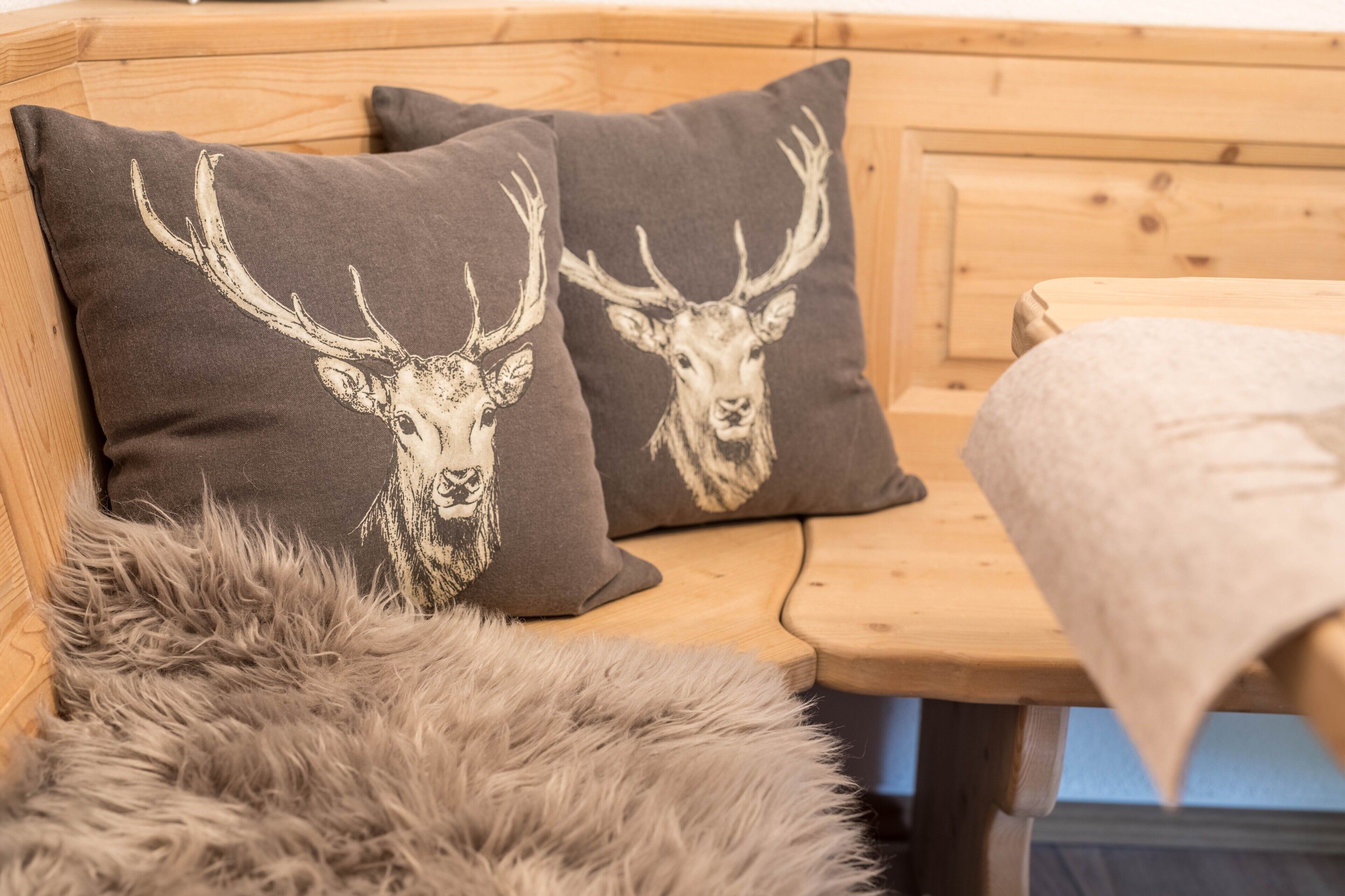 A wooden bench with two pillows featuring deer head prints, a fur throw, and a wooden headboard.