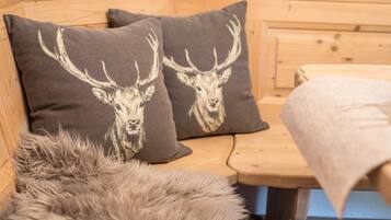 A wooden bench with two pillows featuring deer head prints, a fur throw, and a wooden headboard.