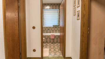 A hallway with a wooden door on the left, a window with blinds, and a patterned floor.