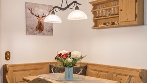 Uma área de refeições com mesa de madeira, assentos tipo banco, um vaso com flores e um candeeiro fixado na parede.
