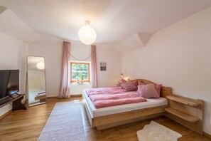 A bedroom with a wooden bed, a TV, a mirror, and a window with curtains.