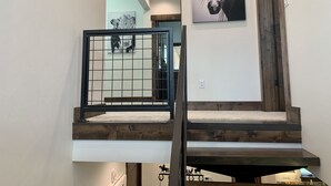 A staircase with wooden steps and a metal railing, leading to a room with a white wall and a horse painting.