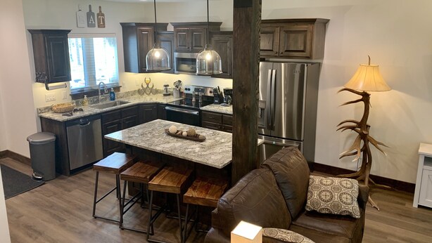 A modern kitchen with dark wood cabinets, stainless steel appliances, and a central island with stools.