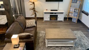 A modern living room with a brown leather sofa, a wooden coffee table, a fireplace, a television, and a ladder against the wall.