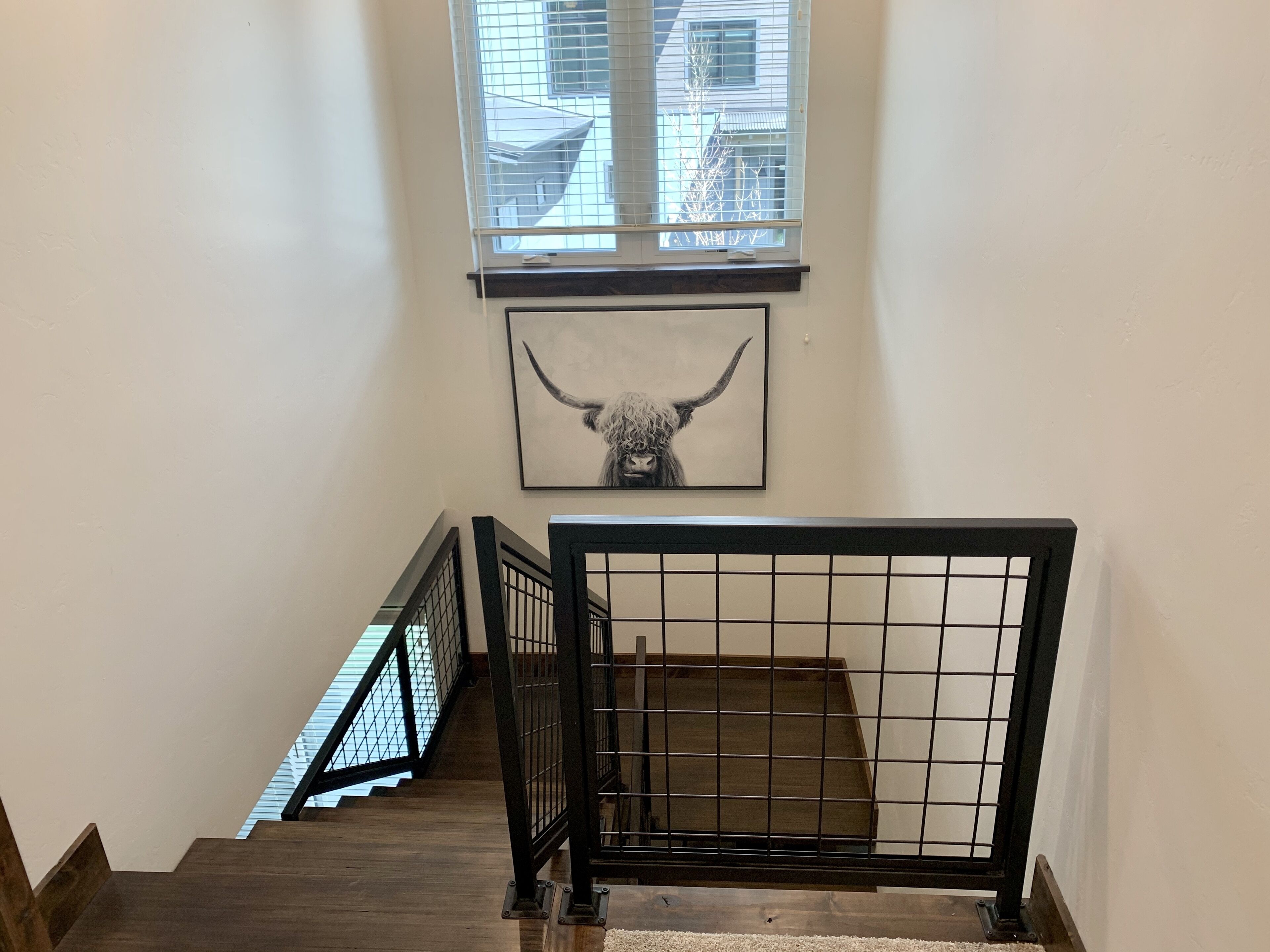 Una escalera con barandilla metálica, una obra enmarcada con la imagen de una cabeza de toro y una ventana con persianas.