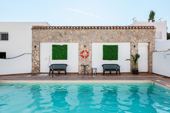 Un espace aménagé au bord de la piscine, avec un muret en pierre, deux bancs, une bouée de sauvetage et une petite table.