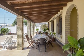 Un patio al aire libre con una mesa lista para comer, rodeada de sillas y un área techada con vigas de madera.