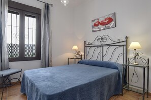 Une chambre à coucher avec un lit, deux tables de chevet avec des lampes, une fenêtre avec des rideaux et un tableau accroché au mur.
